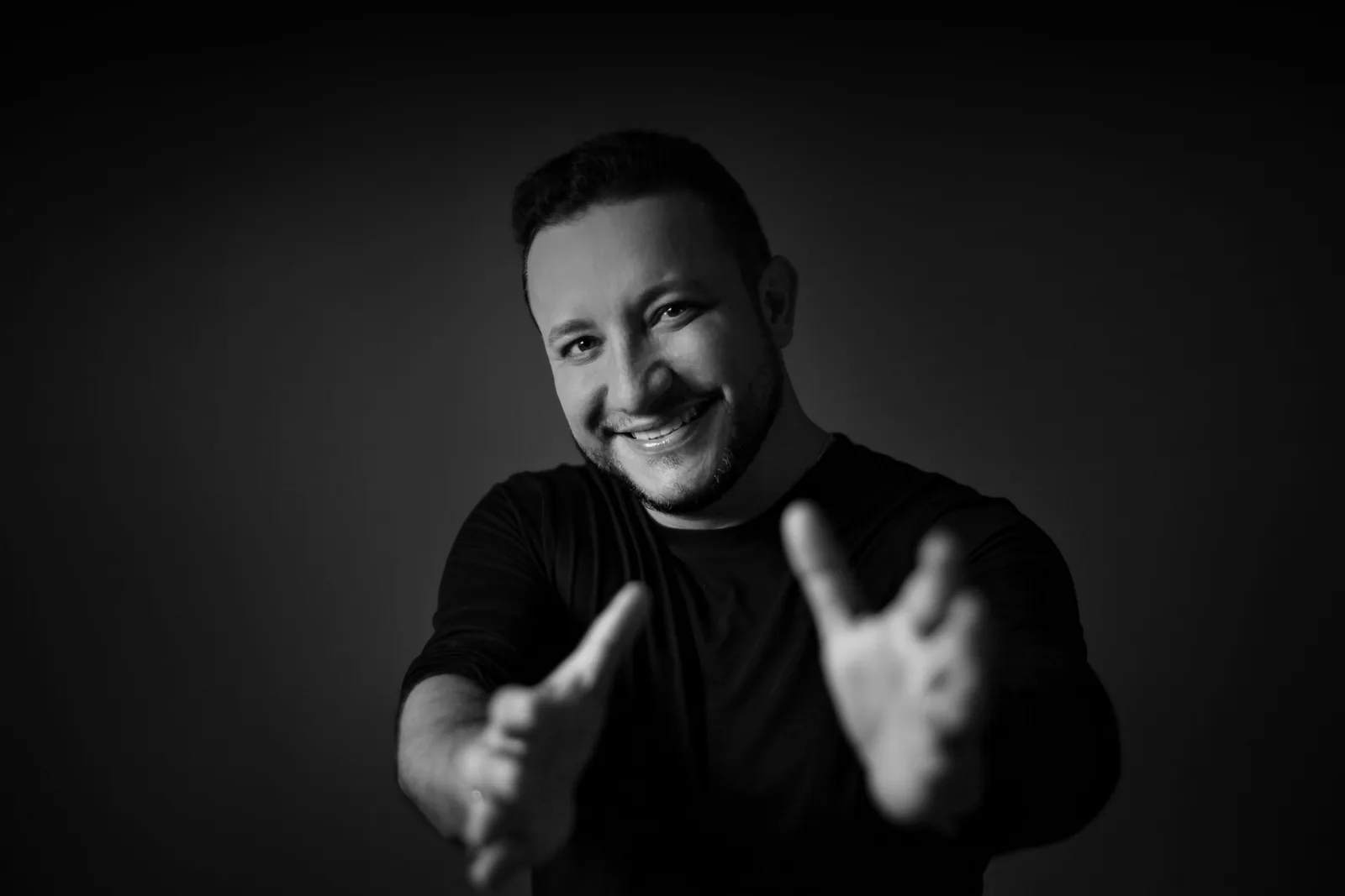 André Oliveira, fundador da CredFácil, sorrindo de braços abertos em retrato preto e branco